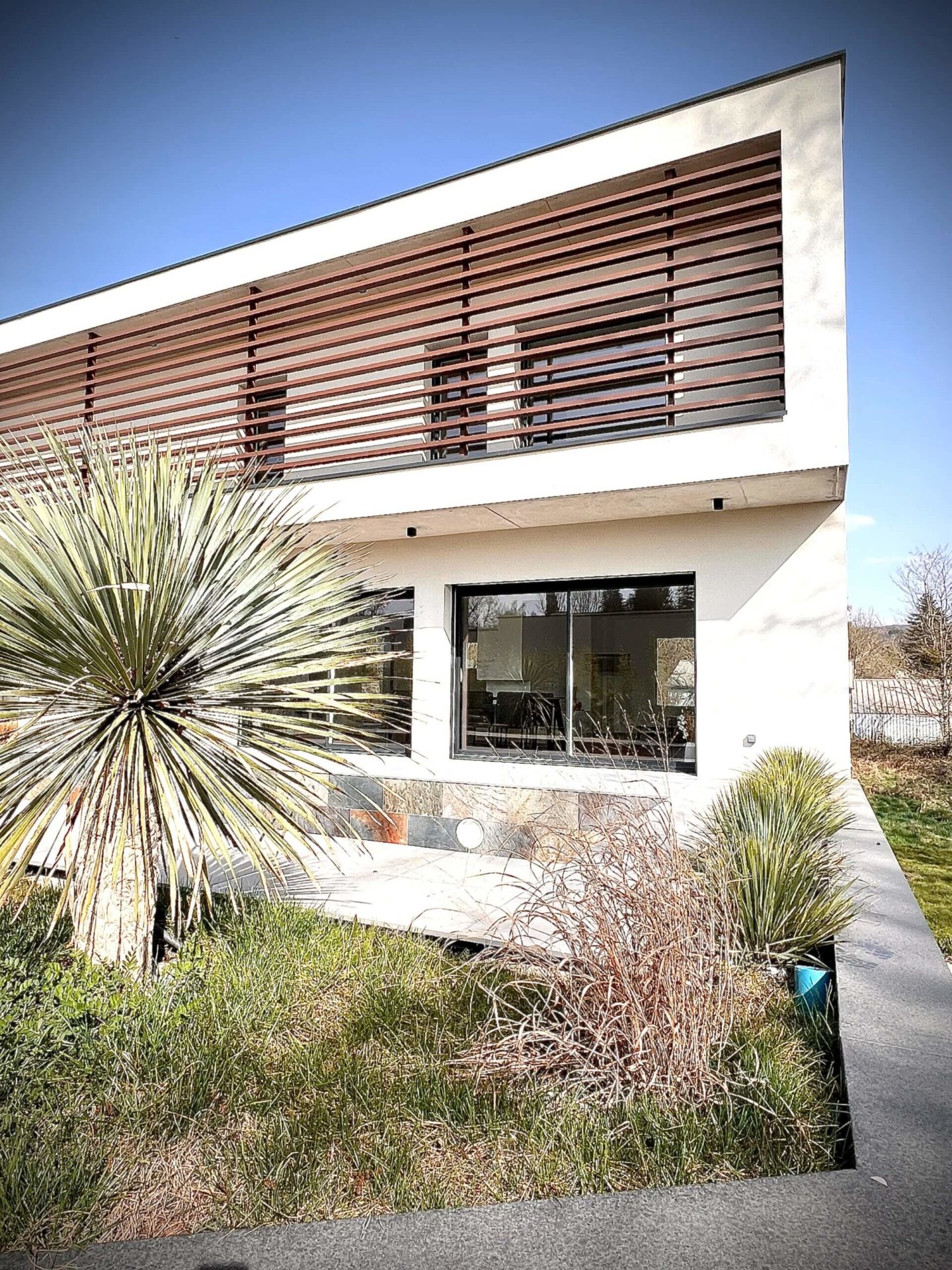 Maison moderne avec végétation sous ciel bleu.