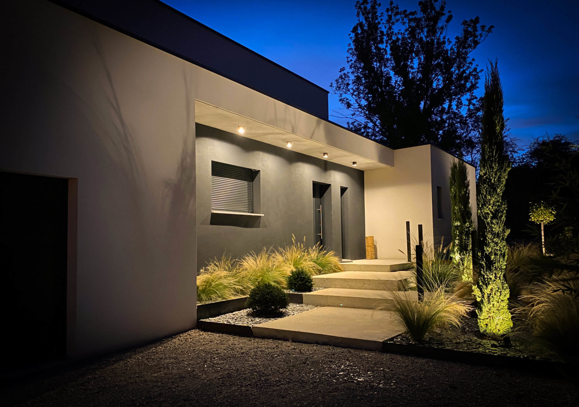 Maison moderne éclairée la nuit avec jardin aménagé.